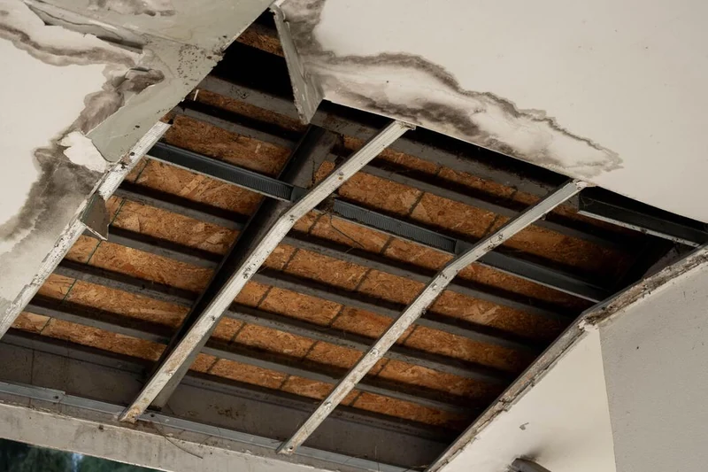 Missing ceiling panels expose framing beneath a water-stained ceiling opening.