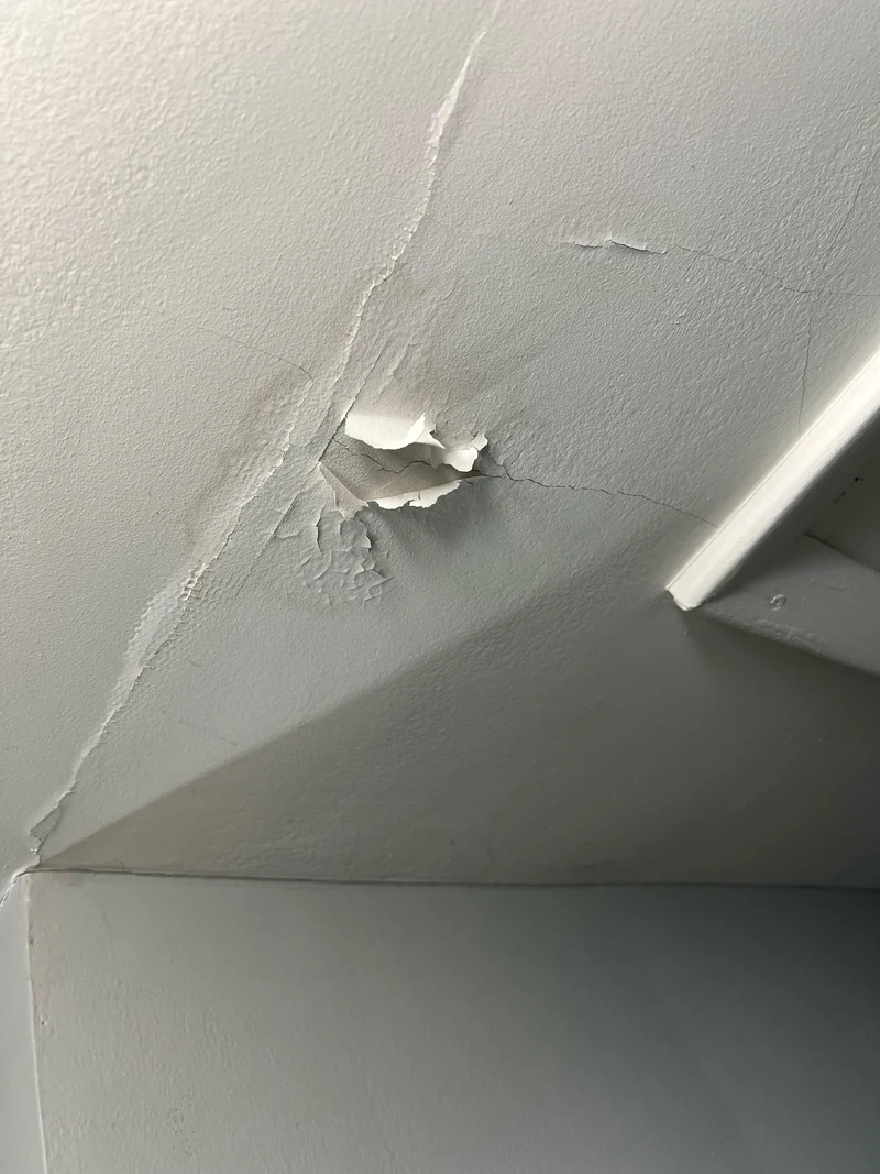 Long ceiling cracks and peeling paint around a damaged joint beside a beam.